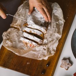 Baker is cutting Christmas baked goods, stollen on a wooden board